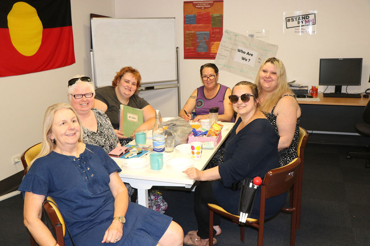 Women First Banner with group of happy women at a table, indigenous flag in background