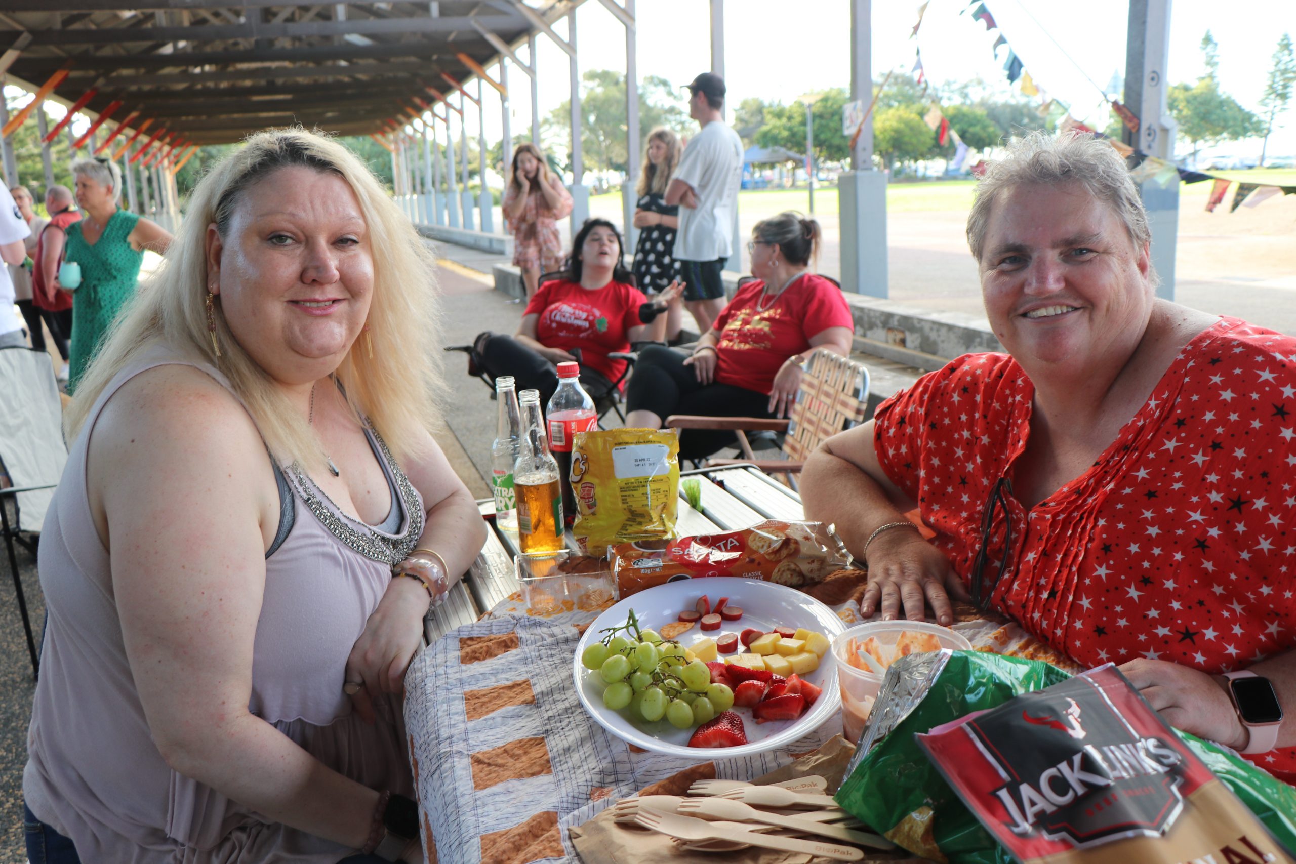 Suzy and Sarah at the christmas party, sitting down at the table with food and drinks. Other people in the background