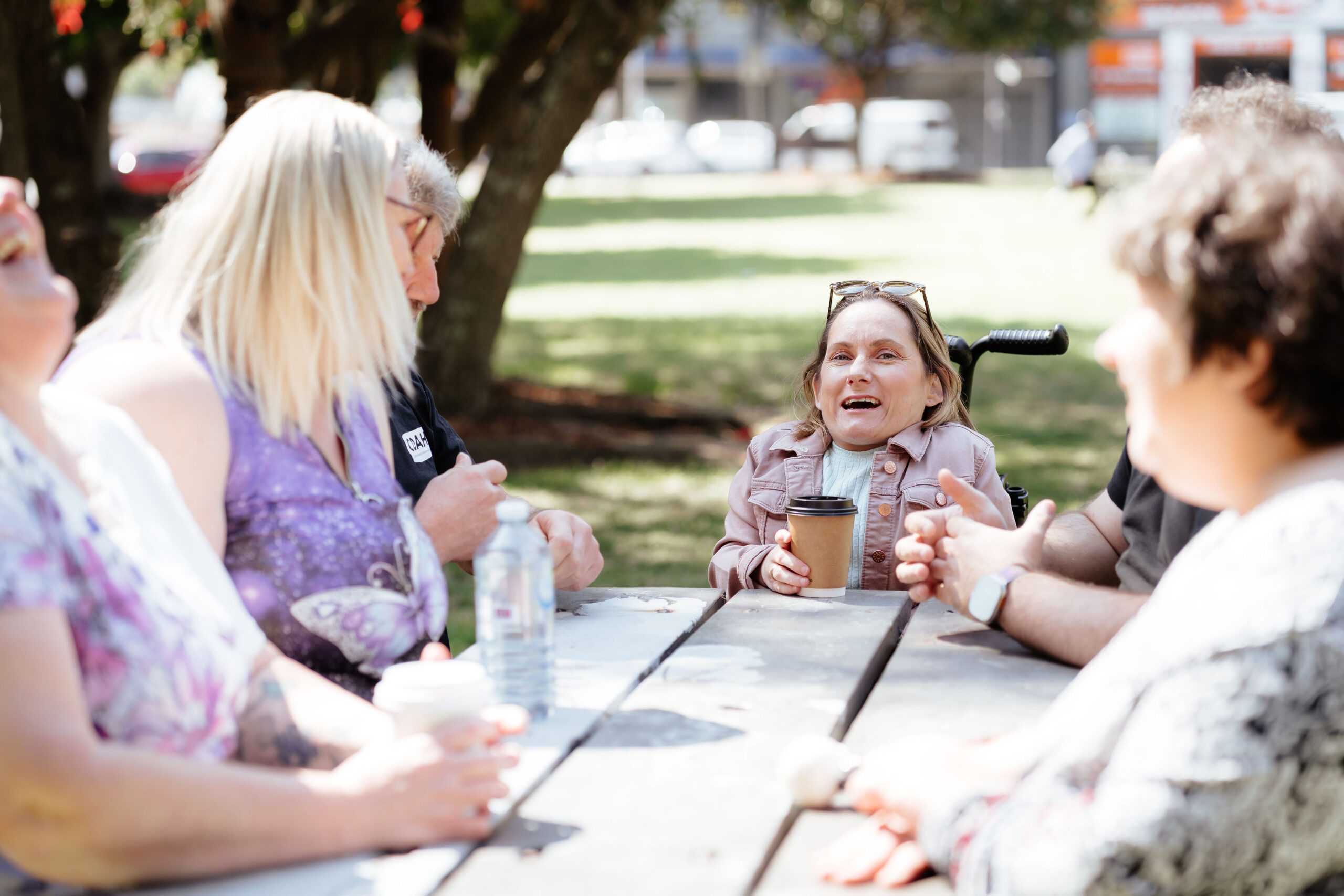 Image description: Group of CDAH peers sitting around table in shady park