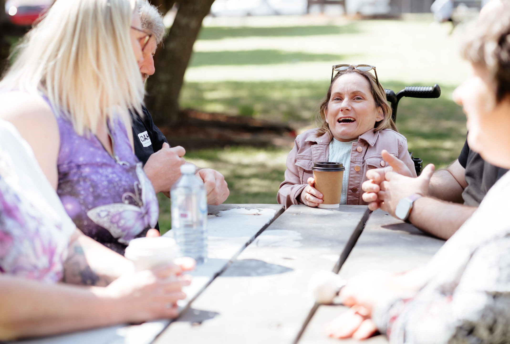 Image description: Group of CDAH peers sitting around a picnic table in shady park
