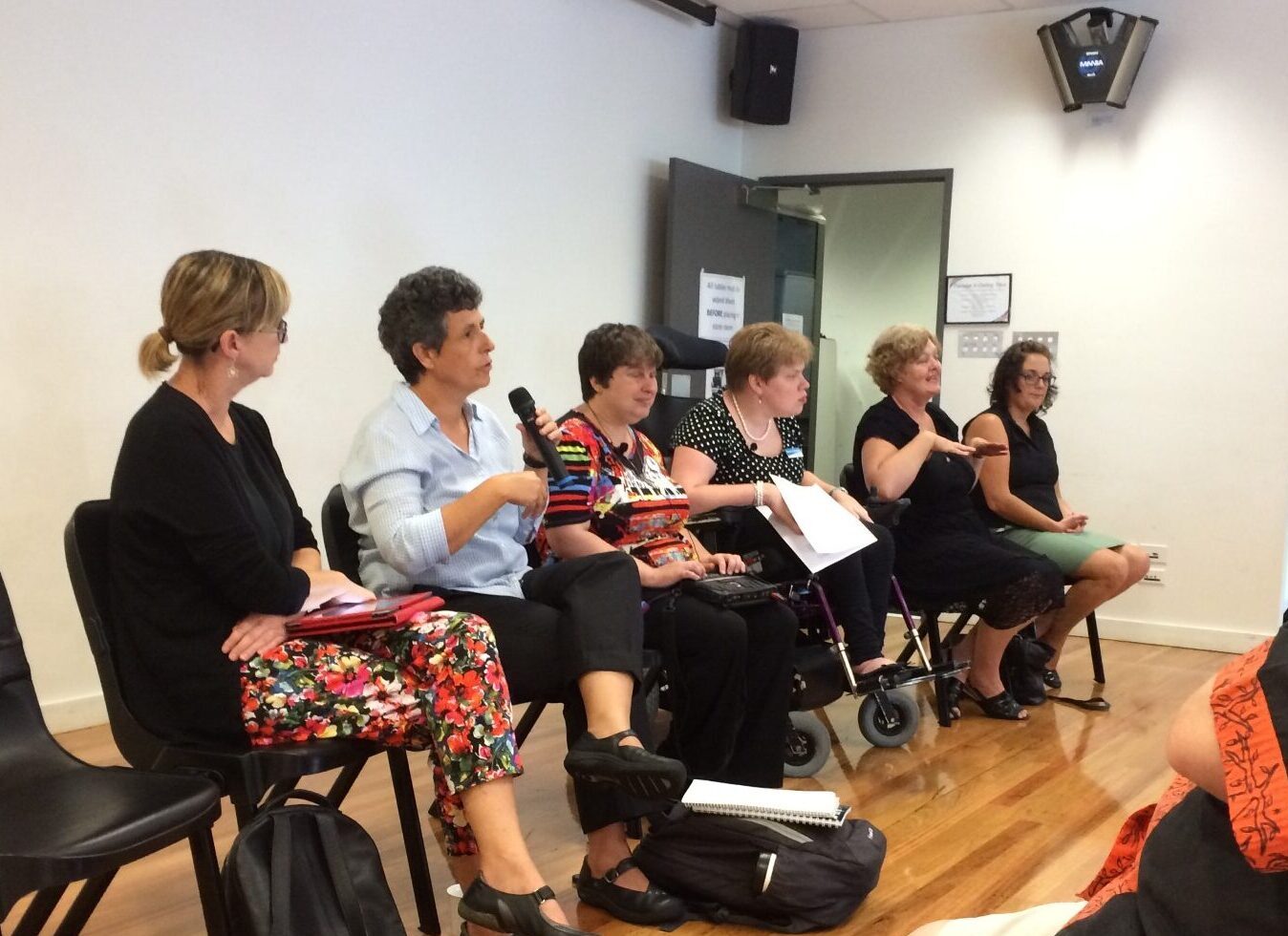 Image description: Six women sitting in a row, speaking to an audience