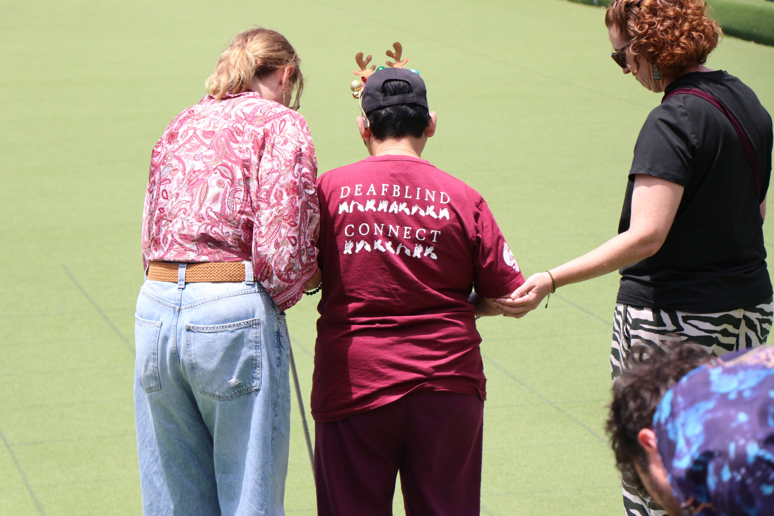 Image description: Three people from Hunter Deafblind connect playing lawn bowls